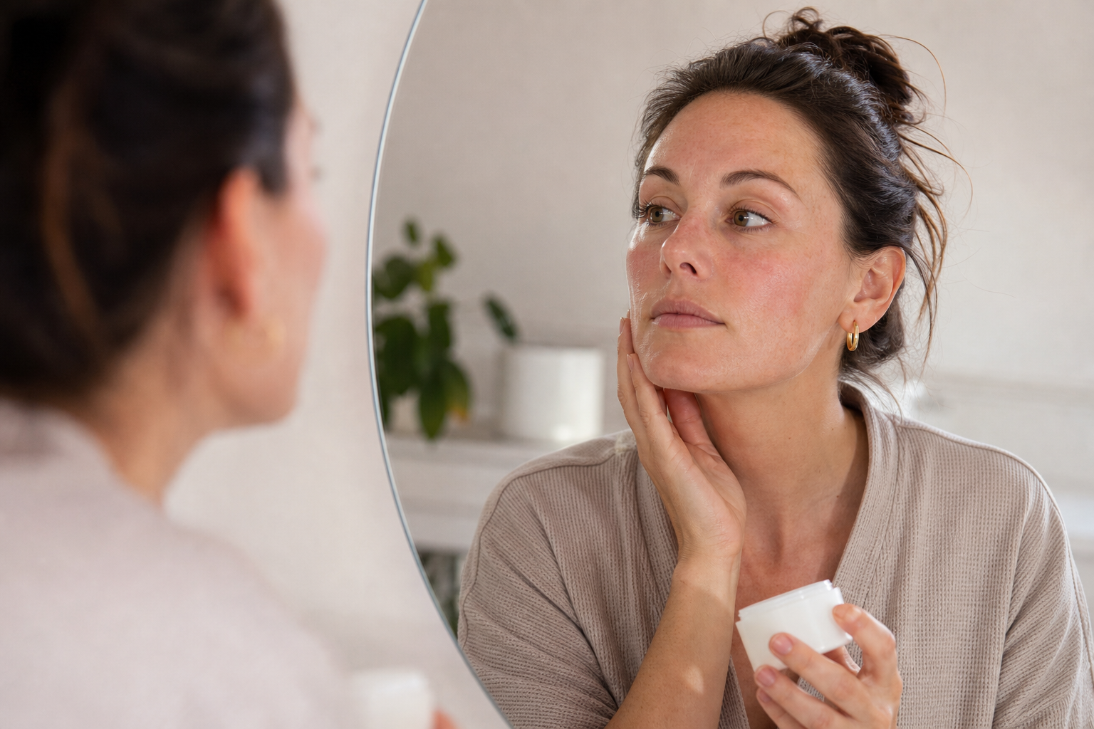 American woman checking calm but sensitive skin in the mirror while holding a simple moisturizer before restarting retinol