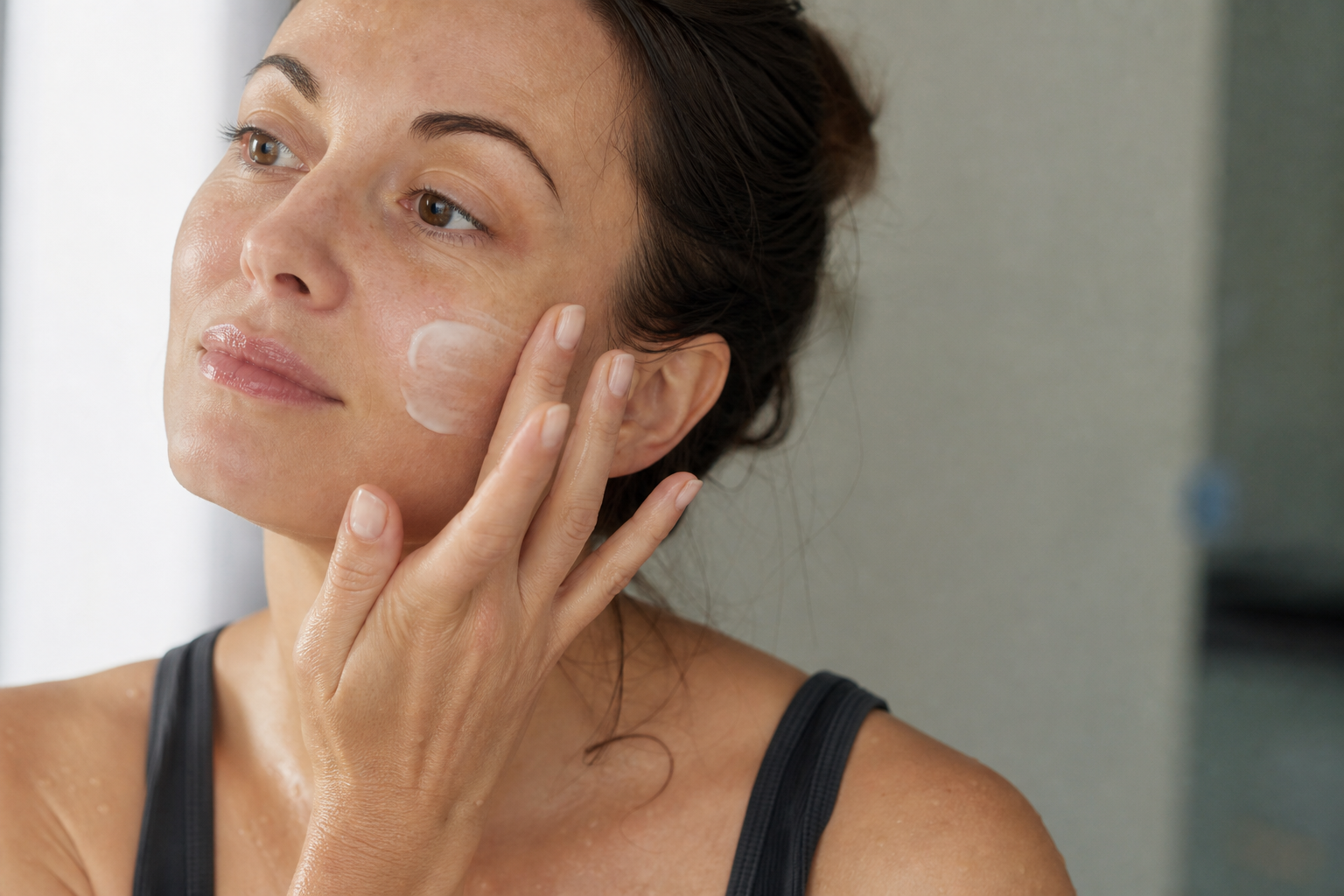 American woman applying plain fragrance-free moisturizer onto slightly damp skin after a gentle cleanse