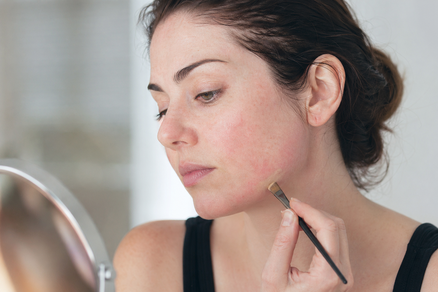 American woman patch testing base makeup along her jawline with a small brush to check for reactive skin
