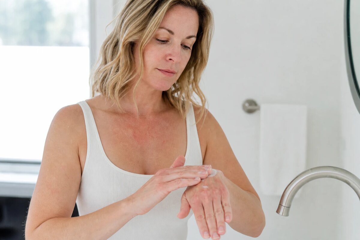 American woman smoothing moisturizer over dry hands after washing at a bright sink