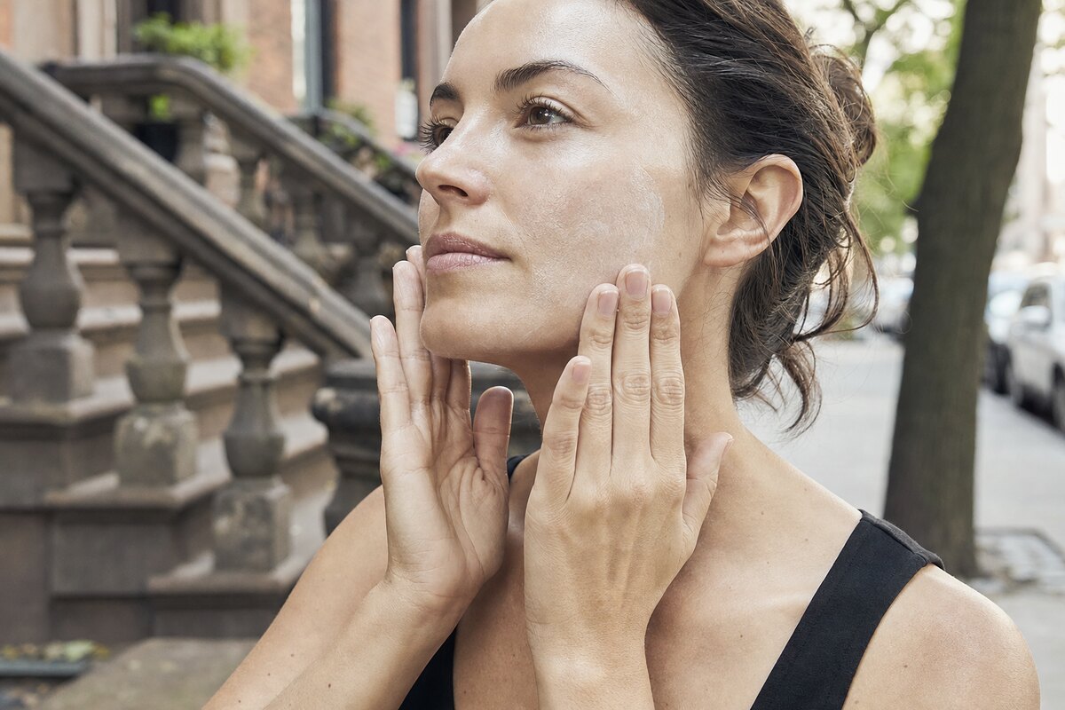 American woman reapplying facial sunscreen outdoors in soft daylight