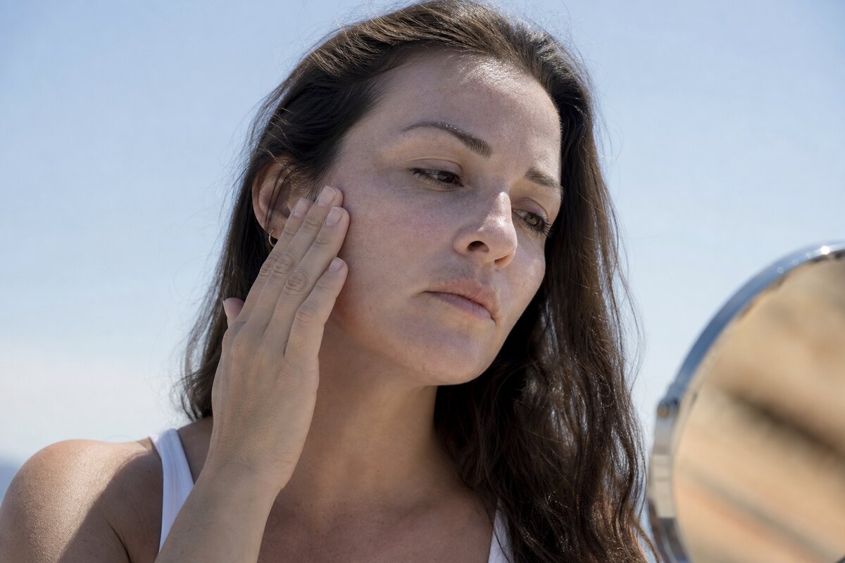 American woman outdoors checking for white cast on her face after applying mineral sunscreen