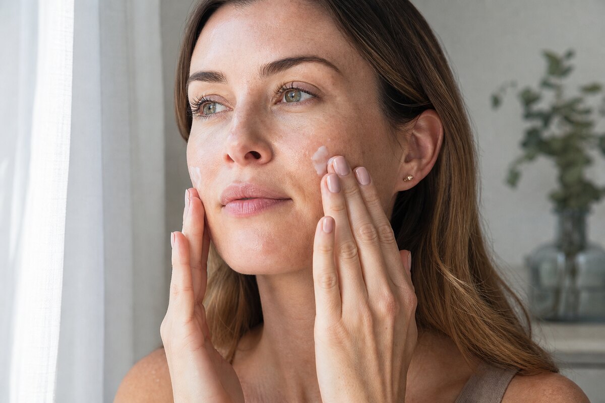 American woman gently pressing moisturizer over a hydrating serum before makeup in soft natural light